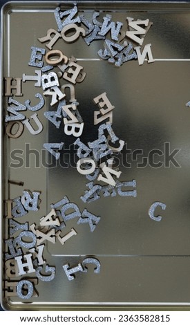wooden letters with silver glitter tops scattered inside a reflective metal lid surface