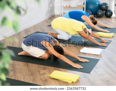 Grandmother, mother and teen son do sitting upside down tree pose, Adho Mukha Virasana in gym. Family three generations keep fit with exercise. Go in for sports. Healthy lifestyle Royalty-Free Stock Photo #2363587731