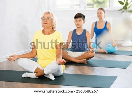 Grandmother, mom and teen son do half lotus position of Ardha Padmasana Sidhasana with hands clasped in mudra of knowledge in gym. Family three generations keep fit with exercise. Healthy lifestyle