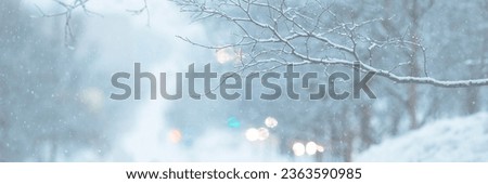 Snow-covered branches and snowflakes in the air. Glittering lights out of focus. Cold winter snowy weather. Evening twilight. Shallow depth of field and blurry background. Wide panoramic background. Royalty-Free Stock Photo #2363590985