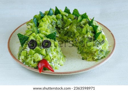 Layered Salad with chicken cheese and kiwi in shape of green Dragon as symbol of chinese new year on a plate on a white table. Creative design for party