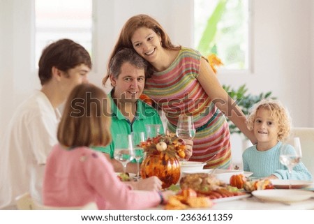 Family with kids eating Thanksgiving dinner. Roasted turkey and pumpkin pie on dining table with autumn decoration. Parents and children having festive meal. Father and mother cutting meat. 