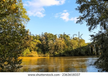 a beautiful autumn landscape along the Chattahoochee River with silky brown water and autumn colored trees, blue sky and clouds at Chattahoochee River National Recreation Area in Sandy Springs Georgia Royalty-Free Stock Photo #2363618337