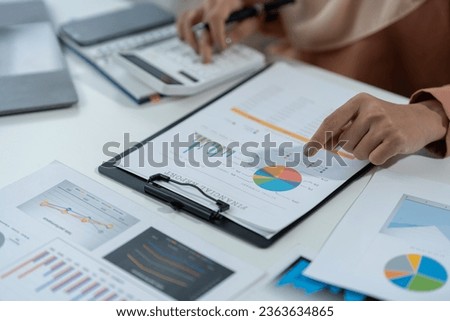 Motivated muslim businesswoman wearing hijab working on real estate project analyzing document data graph discussing presentation work income calculation tax to company in office.