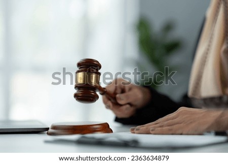 female Muslim lawyer wearing hijab holding the hammer of justice Summary of business contract legal terms in a valid document with investment signing on desk inside the office.