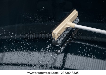 Someone using a glass wiper for cleaning a car windshield. It’s important to keep a car’s front window clear of any visual obstruction for safe driving and to keep the car presentable. Royalty-Free Stock Photo #2363648335