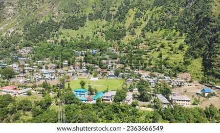 A stunning photo of a small Kashmiri village nestled in the foothills of the Himalayas, India. The village is surrounded by lush green fields and towering snow-capped mountains. Royalty-Free Stock Photo #2363666549