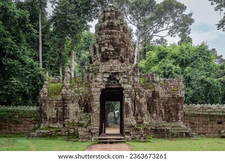 Budda face carved on a moss covered stone building gate at Ta Prohm Tomb Raider temple complex. Angkor Wat historical ruin site Siem Reap, Cambodia Royalty-Free Stock Photo #2363673261