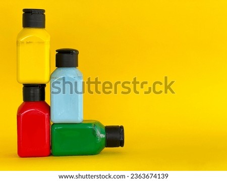 Bottles with bright multi-colored acrylic paint on a yellow background