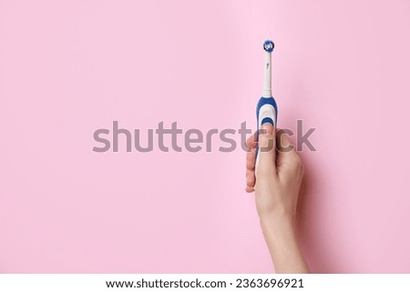 Woman holding electric toothbrush on pink background, closeup. Space for text