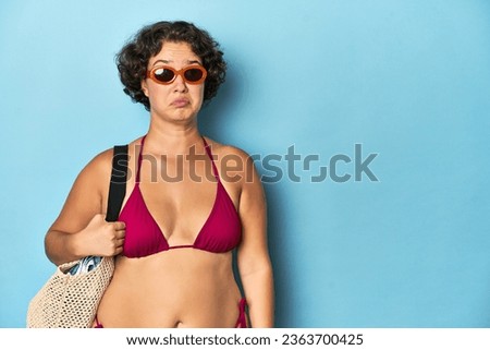 Young woman in bikini with beach bag confused, feels doubtful and unsure.