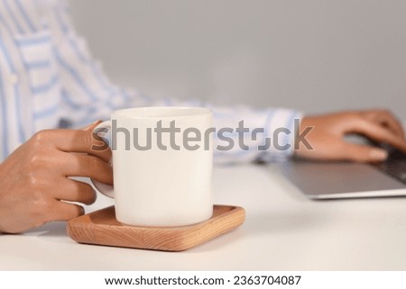 Woman with white ceramic mug at workplace, closeup