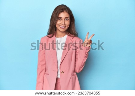 Teen girl in chic pink suit on a blue background showing number two with fingers. Royalty-Free Stock Photo #2363704355