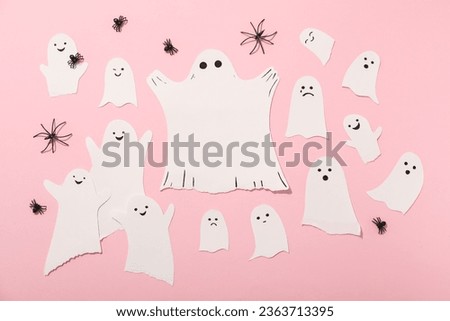 Paper ghosts and decorative spiders on pink background, top view