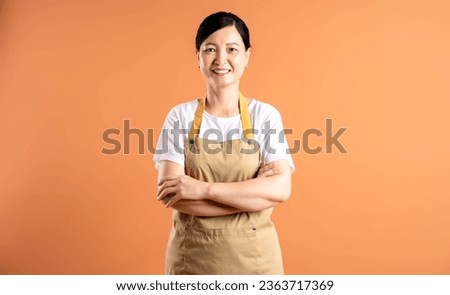 Portrait of Asian female housewife posing on brown background Royalty-Free Stock Photo #2363717369