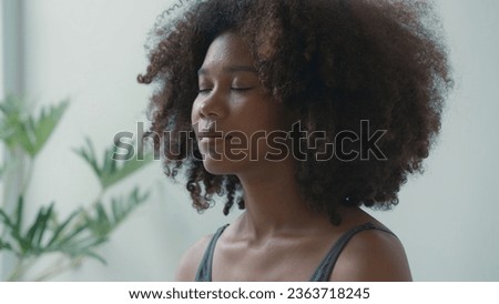 African young adult female engages in a deep meditation or yoga practice at home. With her eyes gently closed, she finds inner peace and calm amidst the demands of daily life. Royalty-Free Stock Photo #2363718245