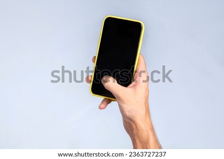 Hand of a man holding a smartphone with his right hand and operating on the screen with his thumb. The phone screen is blank and black, suitable for placing advertisements or pictures. White backgroun
