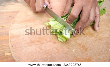 Woman's hands cutting mustard greens using a steel knife, vegetables for cooking, wooden cutting board table background. the results of clean mustard cuttings. stock photo