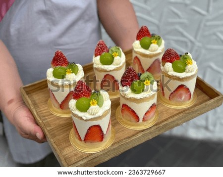 Woman holding plate with delicious Strawberry shortcake. 
Shortcake on a wooden plate. Fresh Strawberry and Shine Muscat topping with cream and yellow flower. Bakery picture free space for text.
