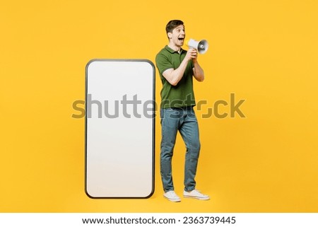 Full body side view young happy man he wears green t-shirt casual clothes big huge blank screen mobile cell phone smartphone with workspace area scream in megaphone isolated on plain yellow background