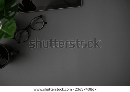 A copy space for displaying your text on a dark grey background with eyeglasses, a coffee mug, a tablet, and a potted plant. top view