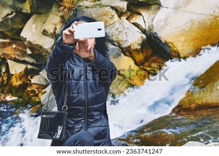 A young woman takes a selfie near a rocky mountain river with a rapid flow                                Royalty-Free Stock Photo #2363741247