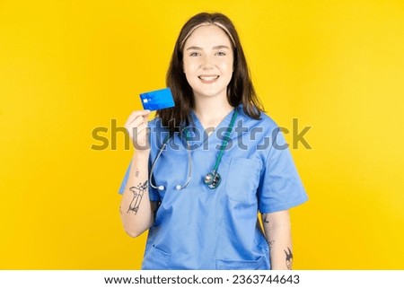 Photo of happy cheerful smiling positive young beautiful doctor woman standing over blue  background recommend credit card