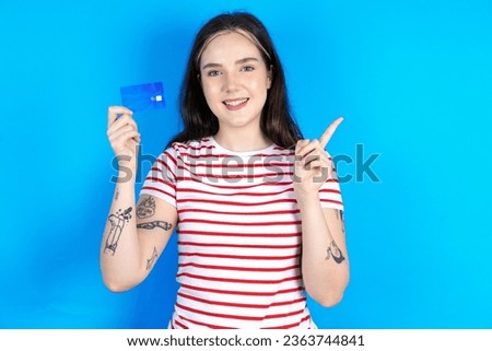 Smiling Young beautiful woman wearing striped T-Shirt showing debit card pointing finger empty space