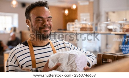 Smiling Man With Down Syndrome Stocking Shelf With Bread In Food Shop