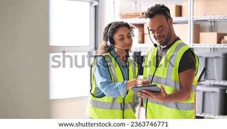 Woman Using Digital Tablet And Male Colleague With Down Syndrome In Warehouse Wearing Headsets Royalty-Free Stock Photo #2363746771