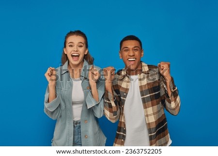 excited interracial couple screaming from joy looking at camera on blue backdrop, emotional reaction Royalty-Free Stock Photo #2363752205