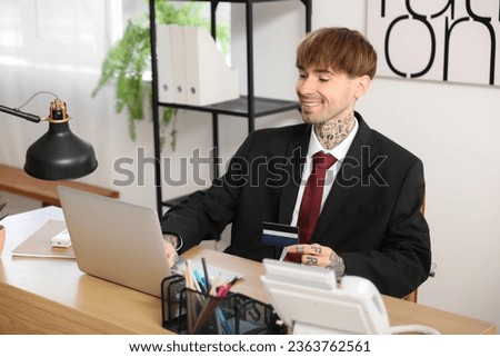 Young businessman with credit card using laptop at table in office