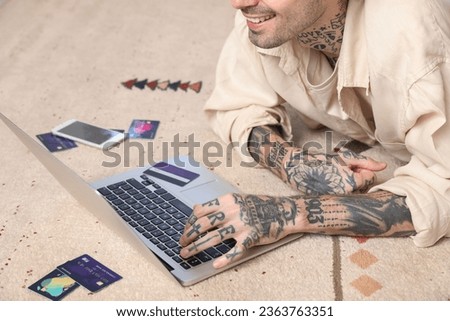 Tattooed young man with credit cards using laptop at home, closeup