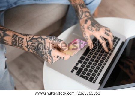 Tattooed young man with credit card using laptop at home, closeup