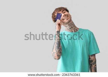 Tattooed young man with credit card on light background