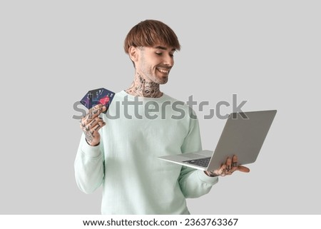 Tattooed young man with credit cards and laptop on light background
