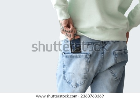 Young man with credit card in pocket on light background, back view
