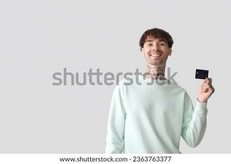 Tattooed young man with credit card on light background