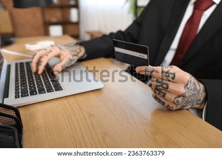 Young businessman with credit card using laptop at table in office, closeup
