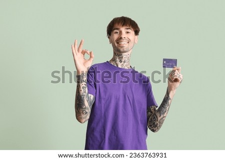 Tattooed young man with credit card showing OK on green background