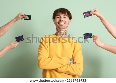Tattooed young man and hands with credit cards on green background