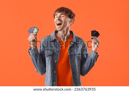 Tattooed young man with credit cards on orange background