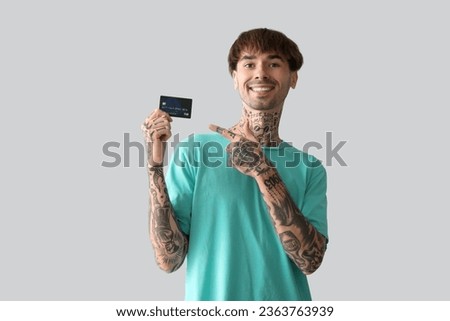 Tattooed young man pointing at credit card on light background