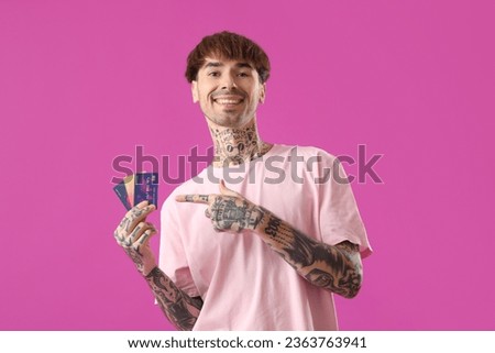 Tattooed young man pointing at credit cards on purple background