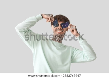 Tattooed young man with credit cards on light background