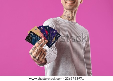 Tattooed young man with credit cards on purple background, closeup