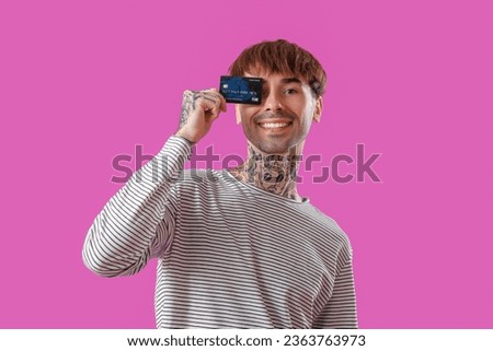 Tattooed young man with credit card on purple background