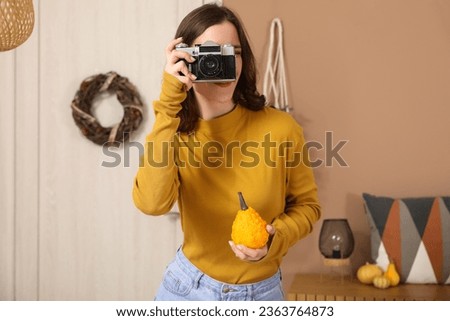 Young woman with pumpkin and photo camera at home on autumn day