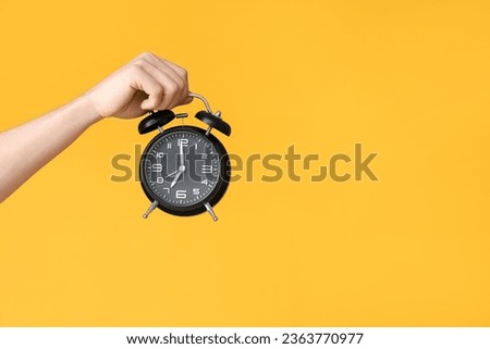 Male hand holding alarm clock on yellow background