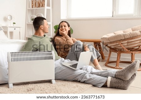 Young couple with laptop warming near radiator in bedroom Royalty-Free Stock Photo #2363771673